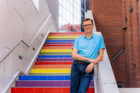 Rector and president Vesa Taatila smiling and standing on rainbow colored stairs.
